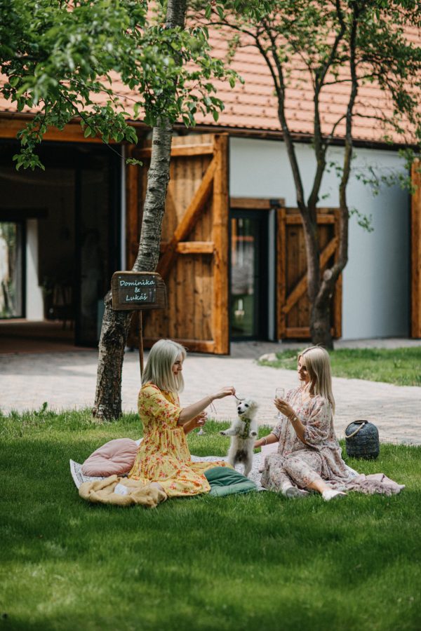 Dvě děti sedící na dece na trávníku u budov statku